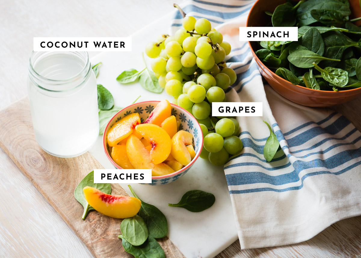 ingredients for a peach spinach smoothie including green grapes, peaches, spinach and coconut water.
