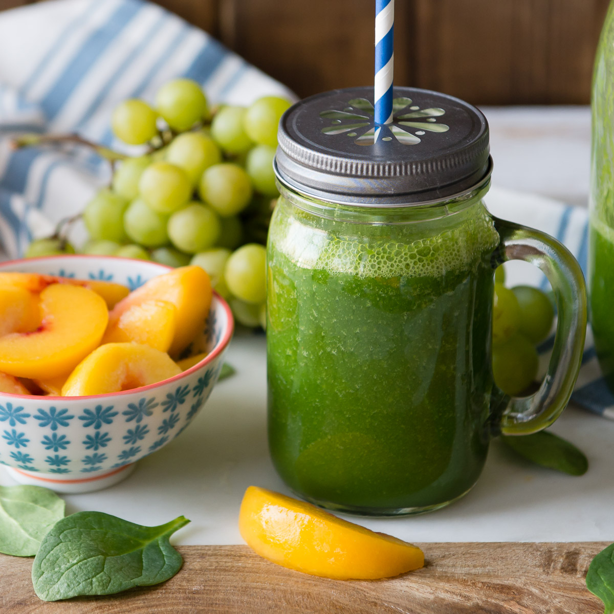 Peach spinach smoothie in a glass Mason jar with a lid and straw next to fresh ingredients
