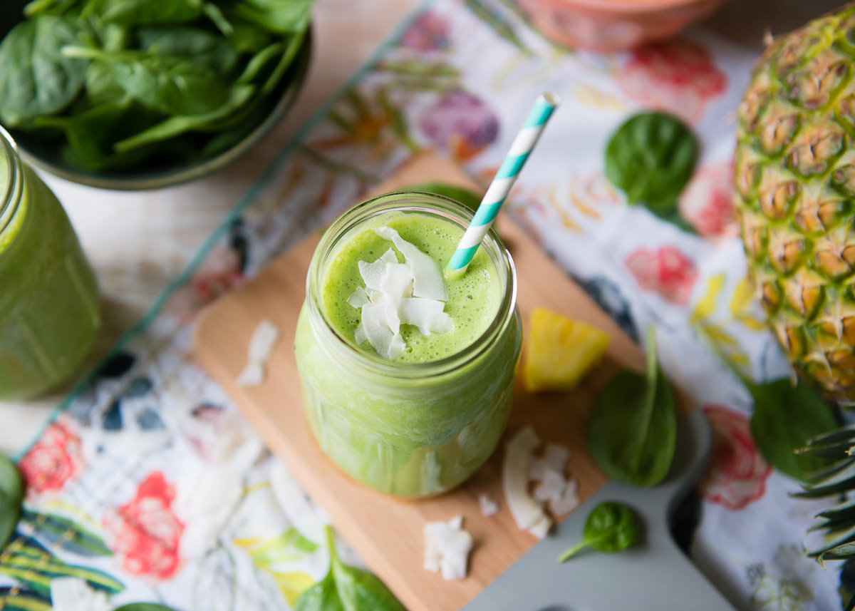 Green Piña Colada smoothie in a Mason jar, topped with coconut slivers, on a festive table with fresh ingredients.