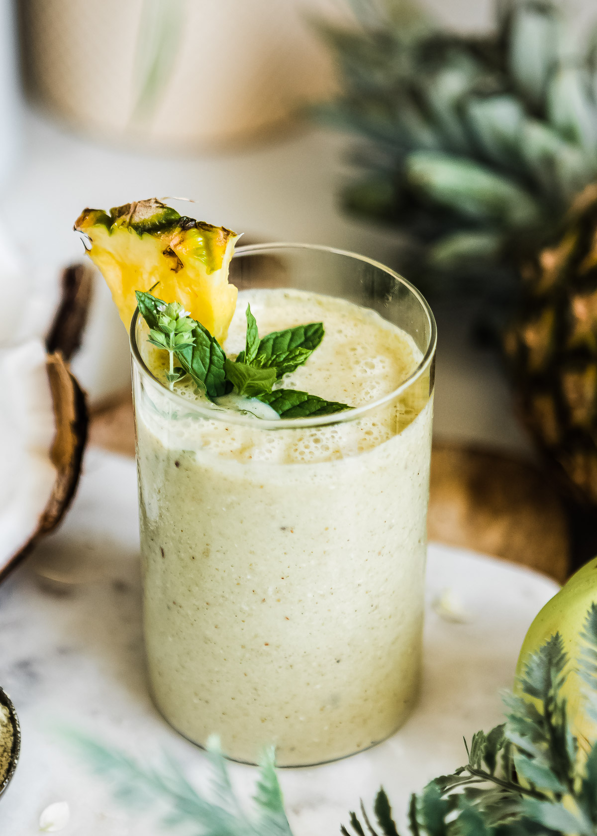 Pineapple banana smoothie in glass with fresh pineapple and mint on top