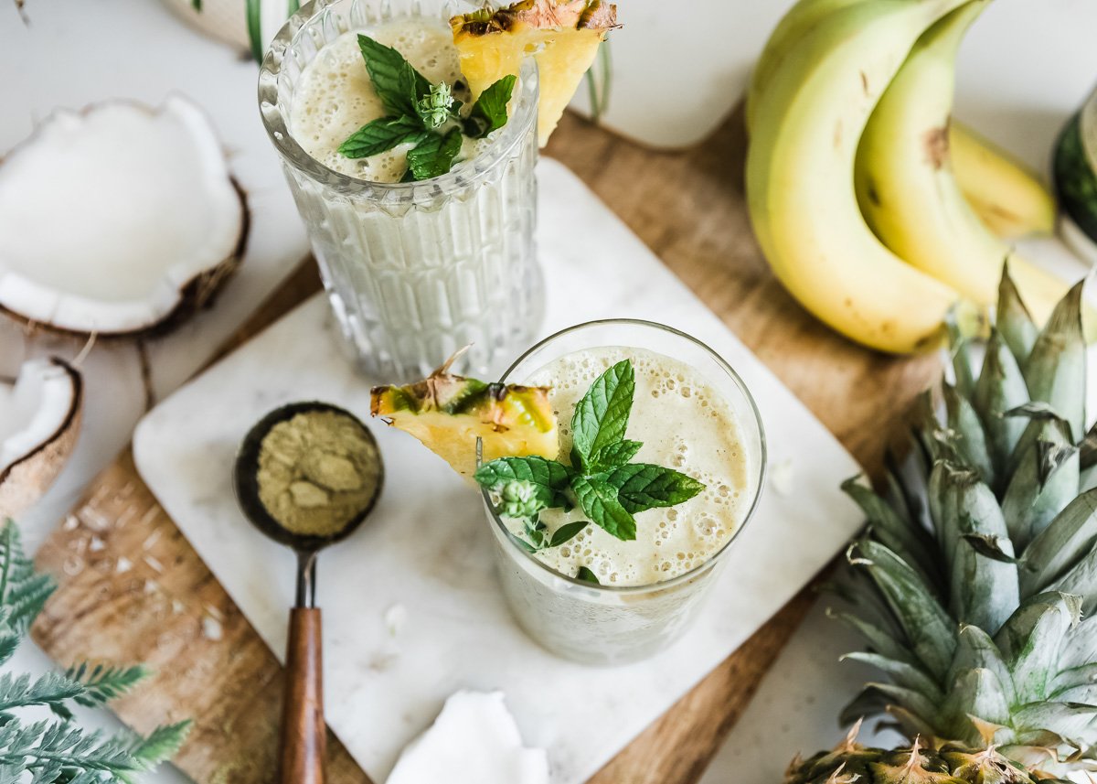 Two glasses of smoothies, each garnished with a pineapple slice on the rim and a sprig of fresh mint