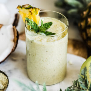 Pineapple banana smoothie in glass with fresh pineapple and mint on top.
