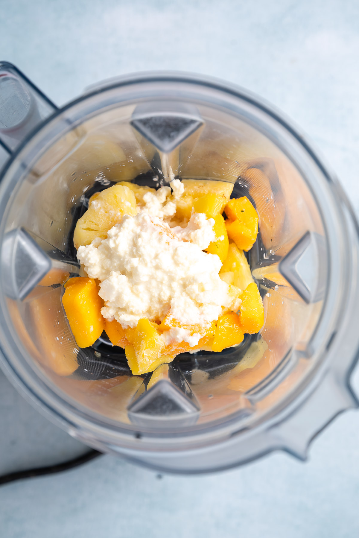 A blender containing cottage cheese and frozen fruits
