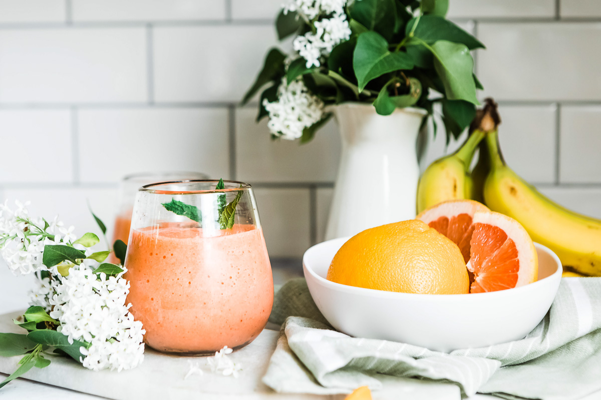 A refreshing glass of pink grapefruit smoothie next to a white bowl filled with grapefruit.