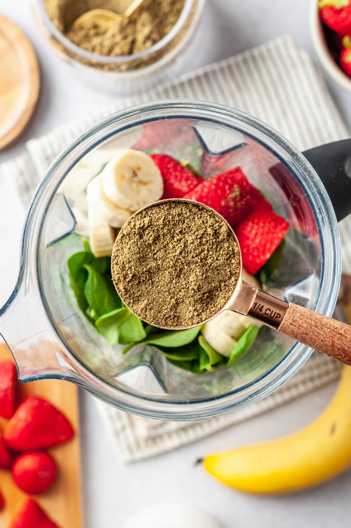 Overhead view of homemade protein powder being poured into a blender container with fruit.