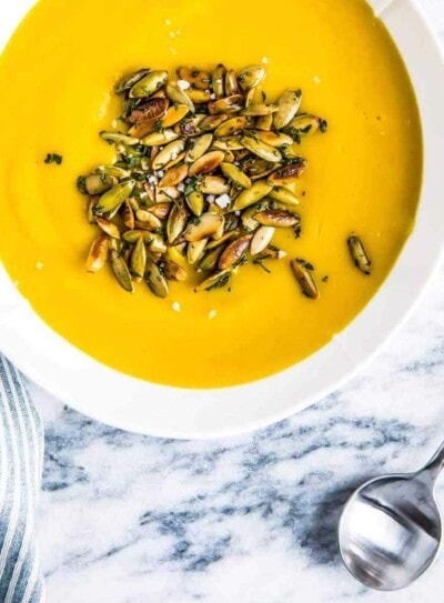 white bowl full of vegan pumpkin soup topped with roasted pumpkin seeds, on a marble counter top.