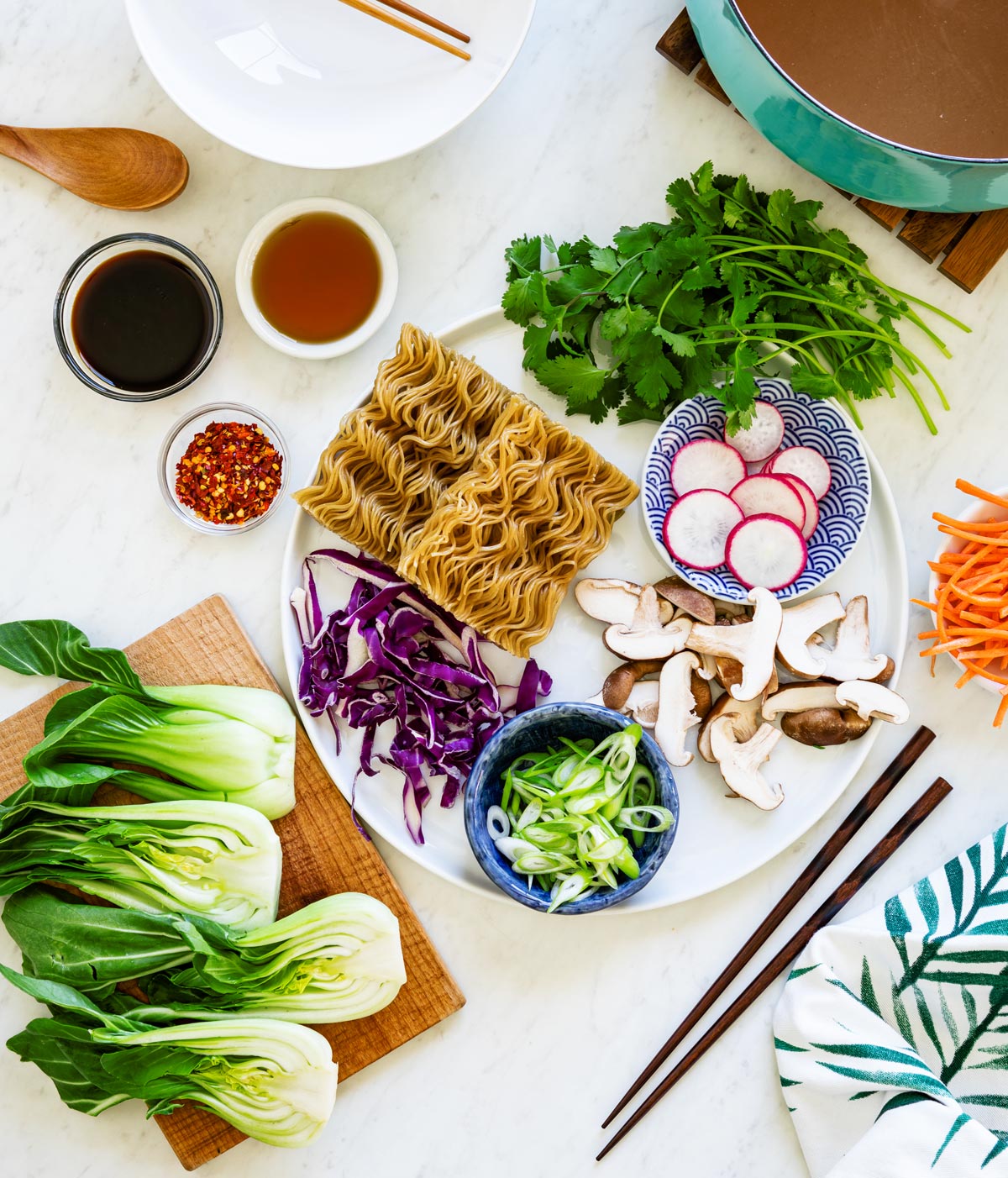 Blue stock of vegetable stock next to a white tray of fresh vegetables to make vegetarian ramen recipe.