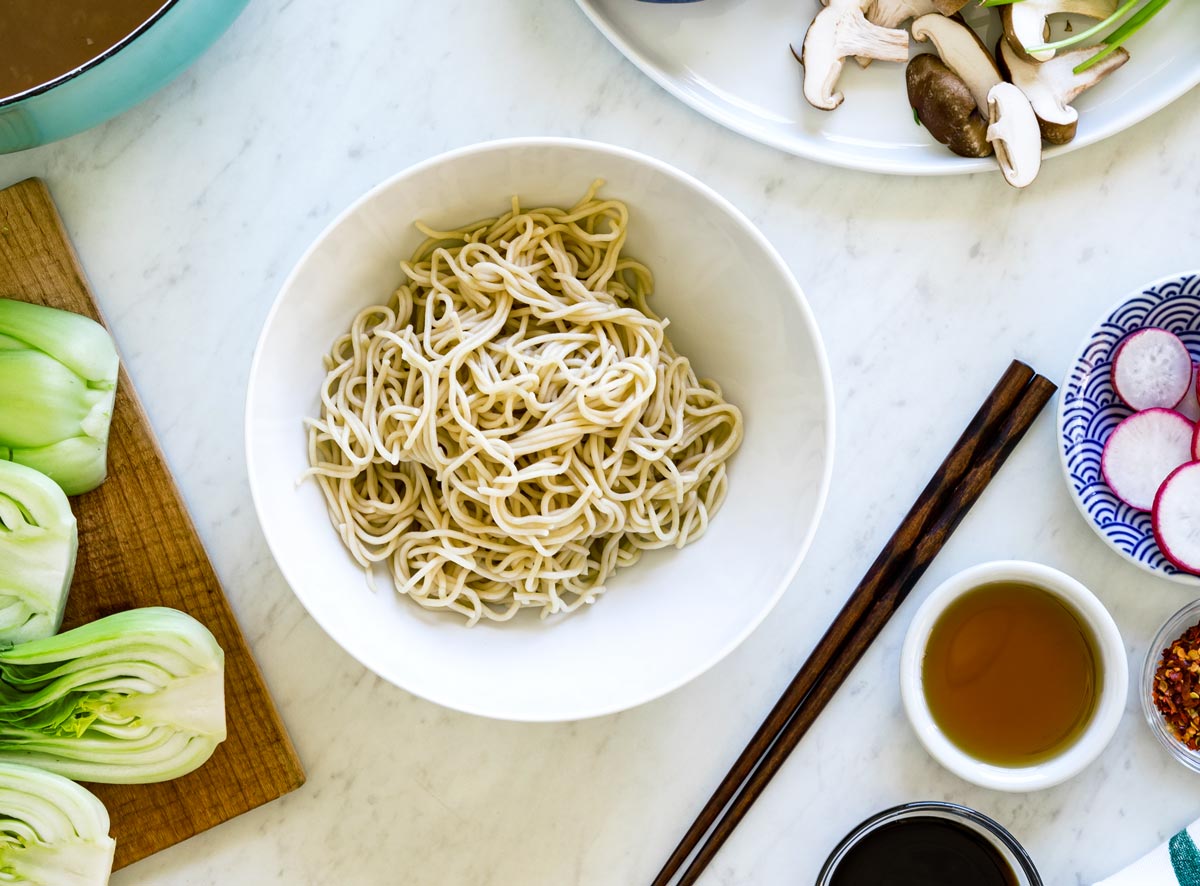 Instant ramen noodles sitting in white bowl with ramen vegetable toppings surrounding it.