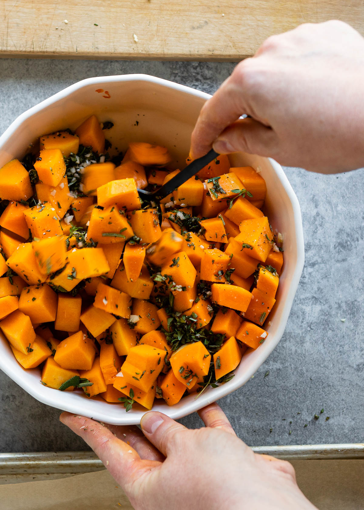 Person mixing roasted butternut squash and herbs with a spoon 