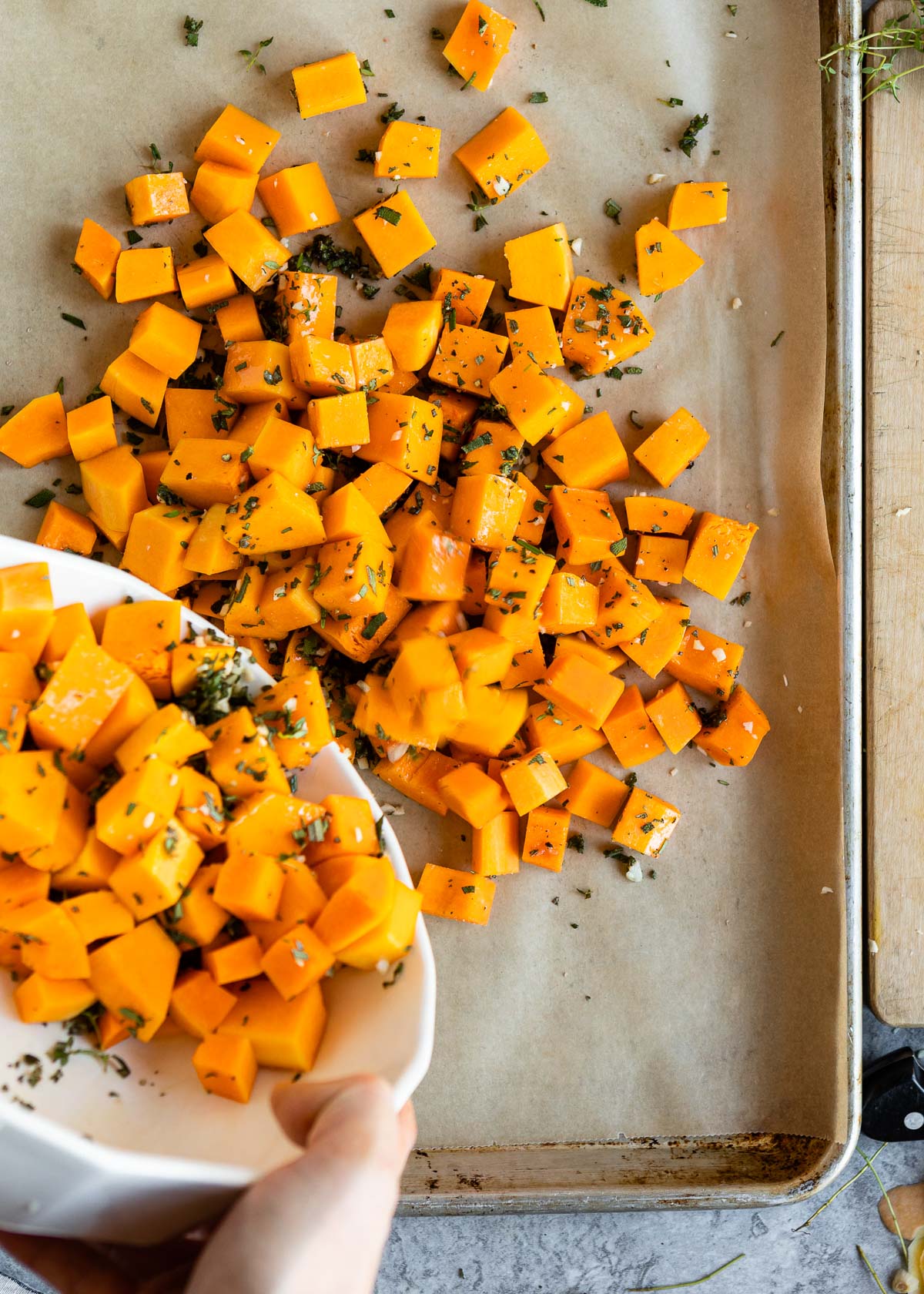 A person pouring diced squash over parchment paper