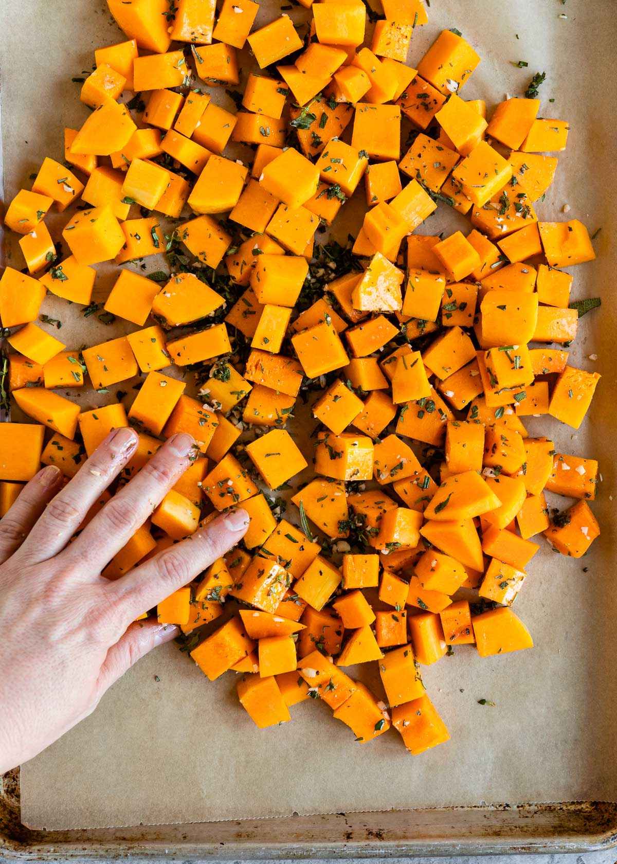 A person spreading diced squash evenly over parchment paper