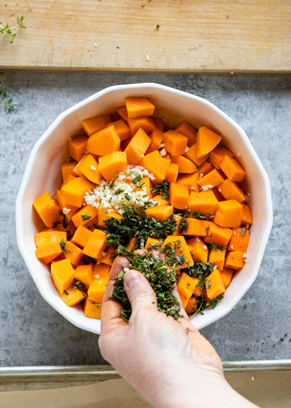 A person adding chopped herbs and garlic on a diced squash