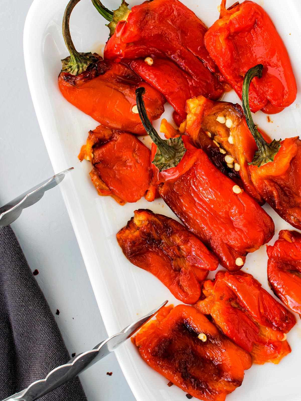 Roasted red bell peppers on a plate with tongs