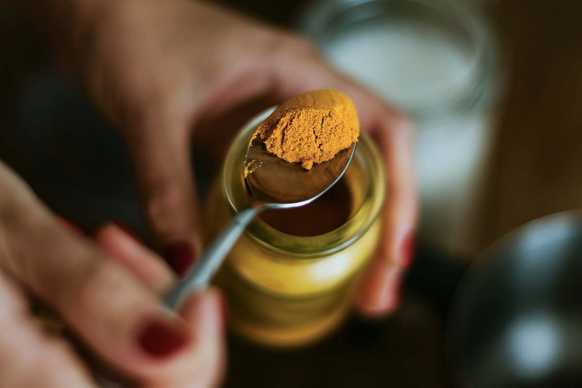 A half spoon of vibrant turmeric powder being scooped from a glass jar