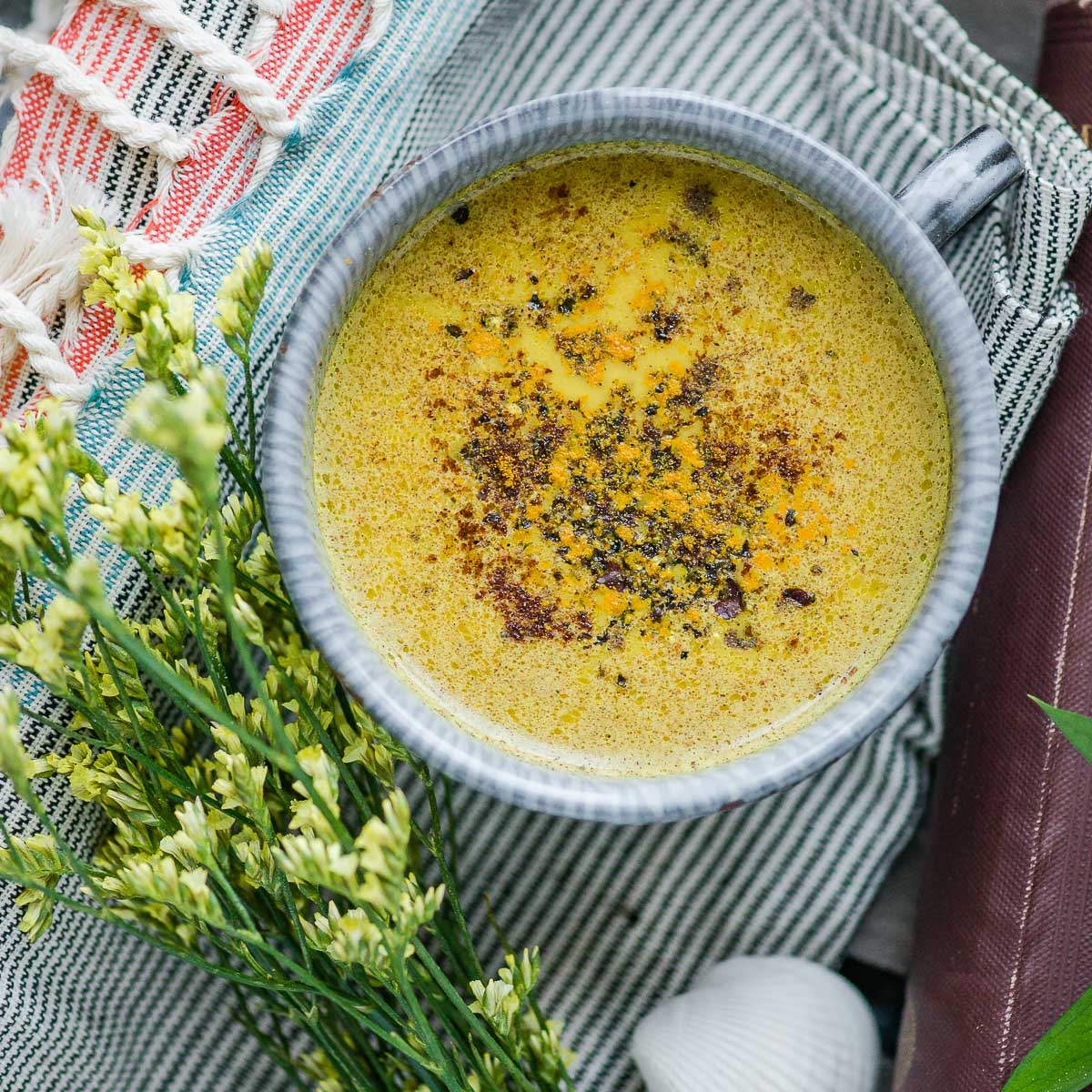 turmeric golden milk in a ceramic mug topped with turmeric and cracked black pepper, sitting on a tea towel.