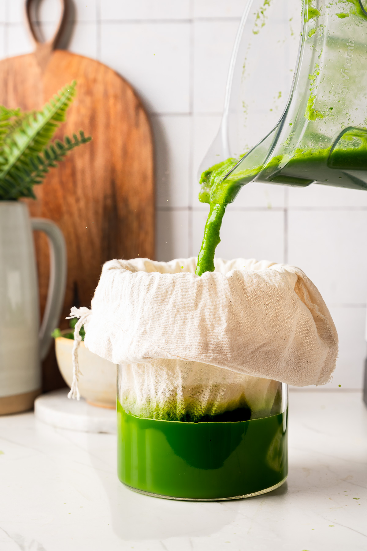 Thick green juice mixture being poured into a white cloth-lined glass jar