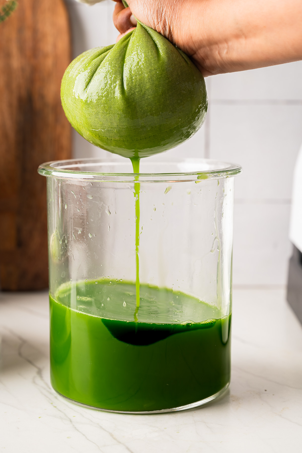 Hands squeezing a white cloth to extract green juice