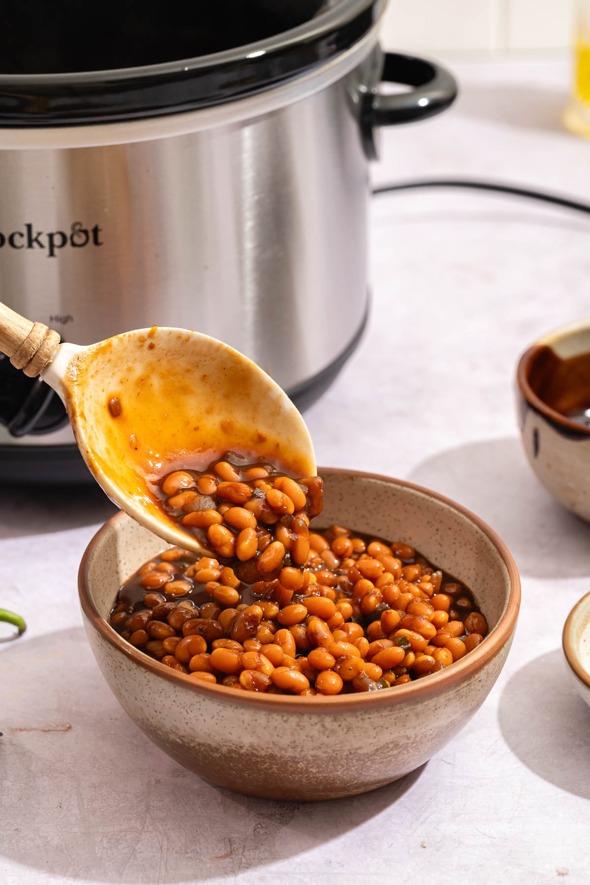 Adding slow cooker baked beans to a bowl for serving