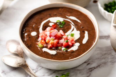 Spicy vegan black bean soup garnished with pico de gallo and vegan sour cream