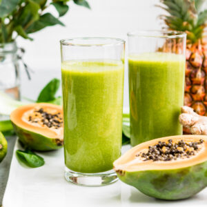 Two tall glasses of creamy papaya spinach smoothie.