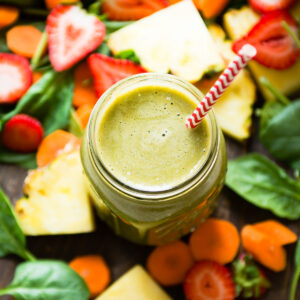 Top-down view of a Mason jar with strawberry carrot smoothie, a red and white straw, and surrounding sliced fruits.