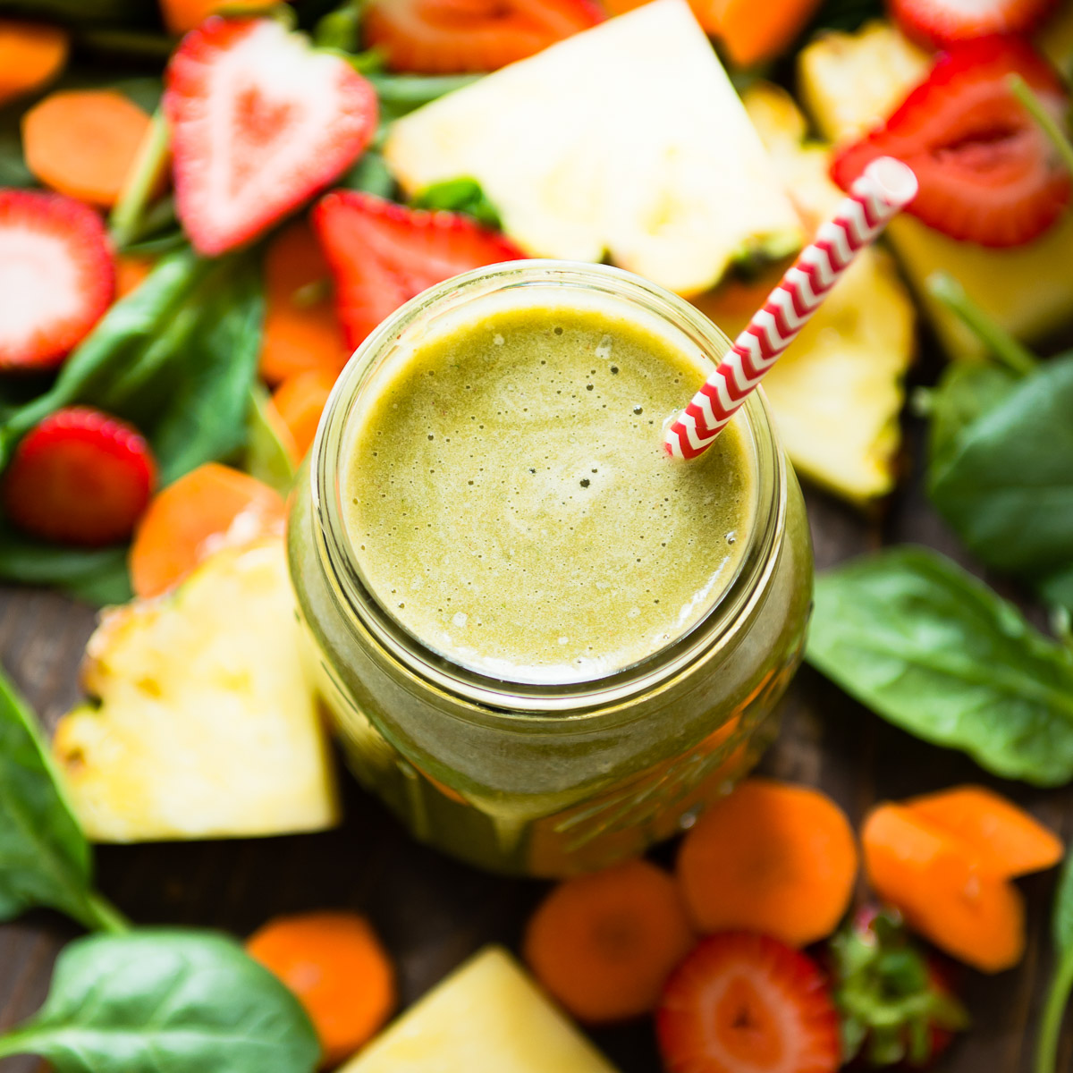 Top-down view of a Mason jar with strawberry carrot smoothie, a red and white straw, and surrounding sliced fruits.