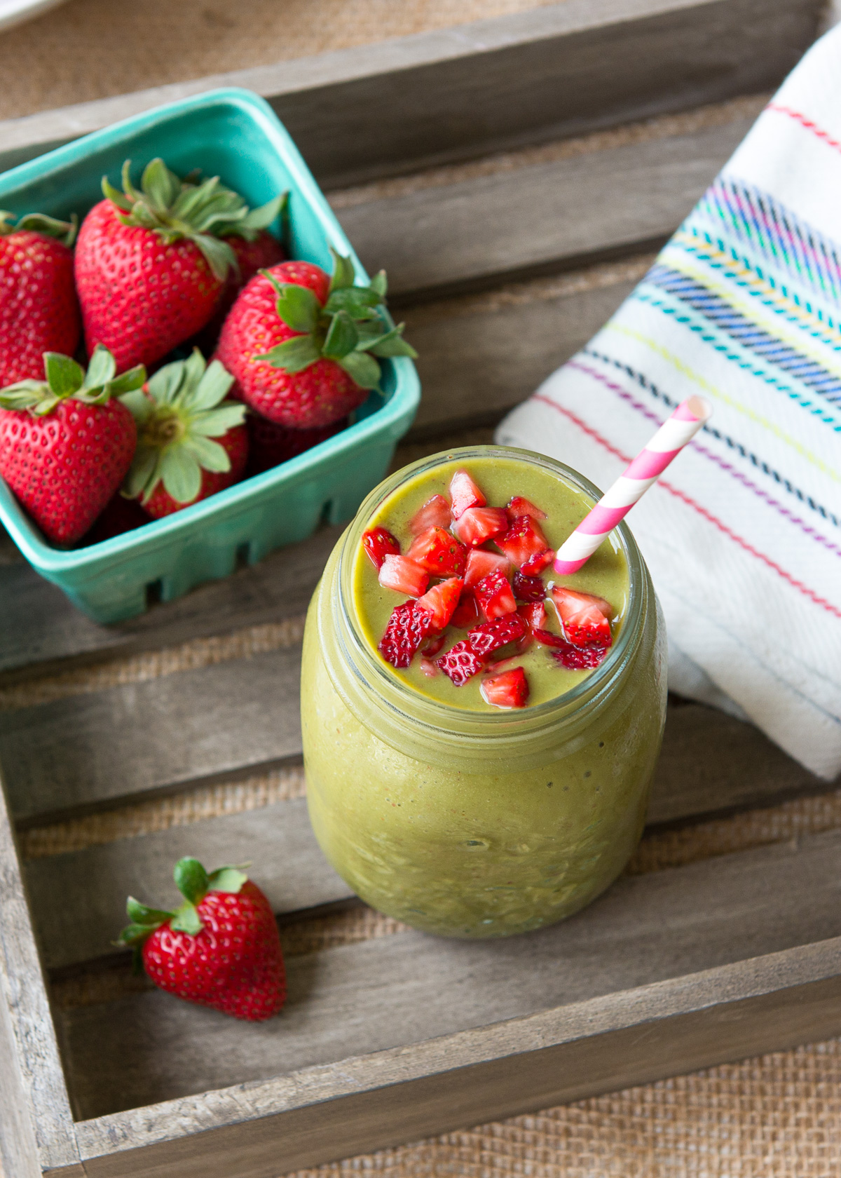 Strawberry mango smoothie sitting in a wooden crate next to a container of fresh strawberries.