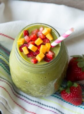 Strawberry mango smoothie in a glass jar with paper straw and fresh fruit.