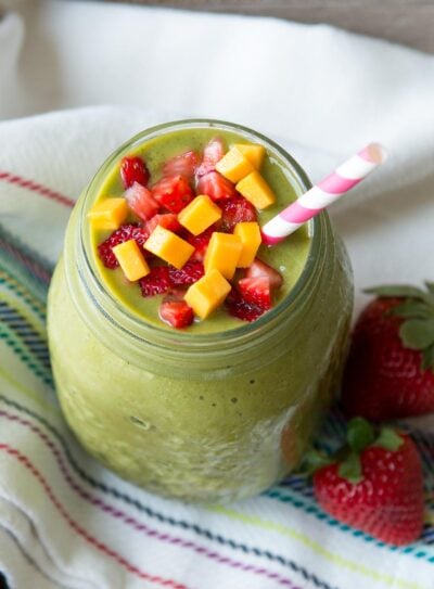 Strawberry mango smoothie in a glass jar with paper straw and fresh fruit.