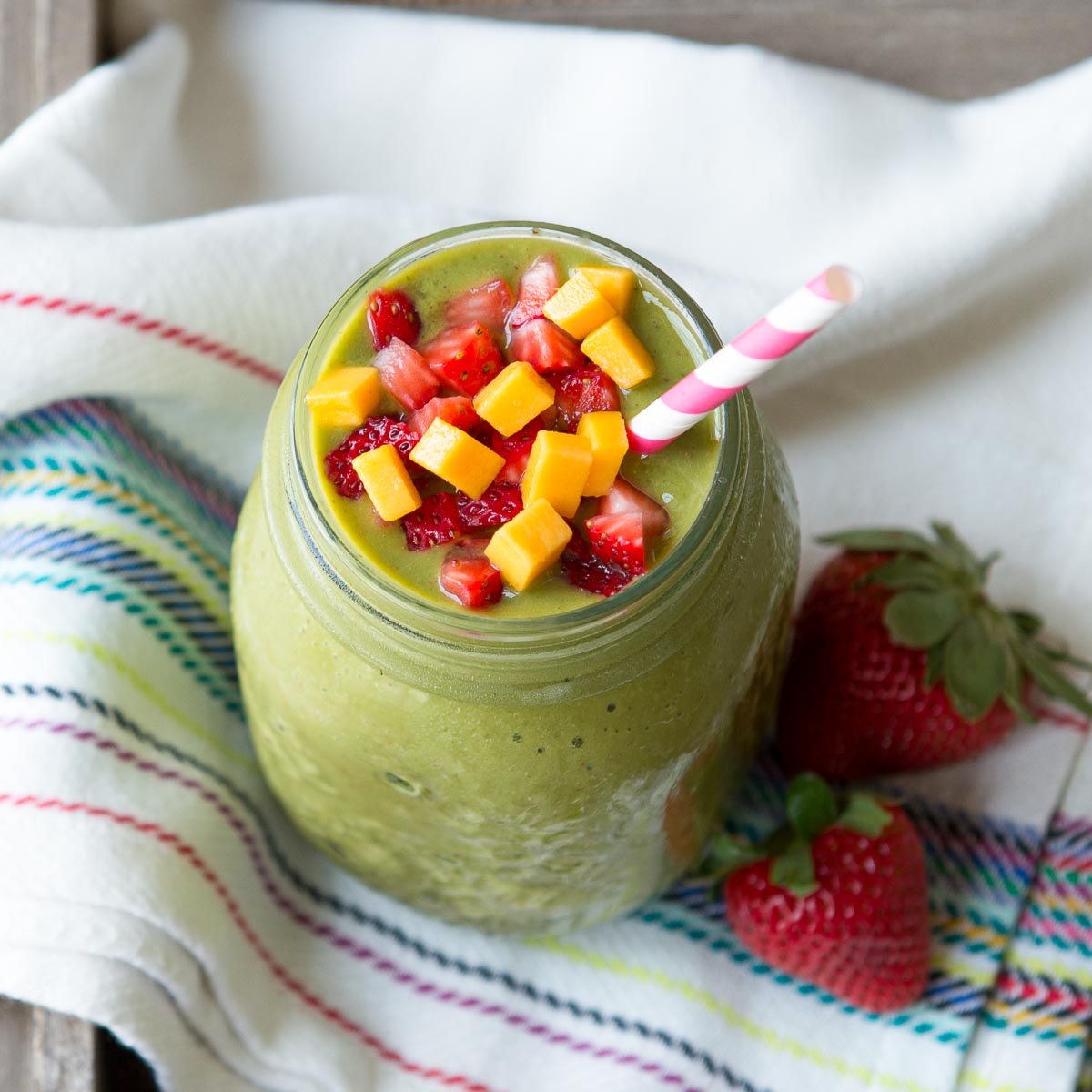 Strawberry mango smoothie in a glass jar with paper straw and fresh fruit.