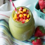 Strawberry mango smoothie in glass jar with paper straw and topped with fresh fruit.