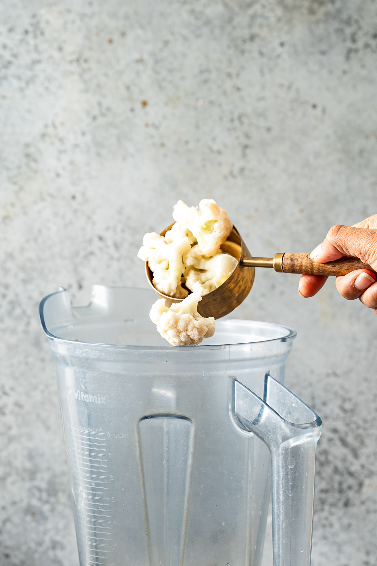A person adding cauliflower florets in a blender