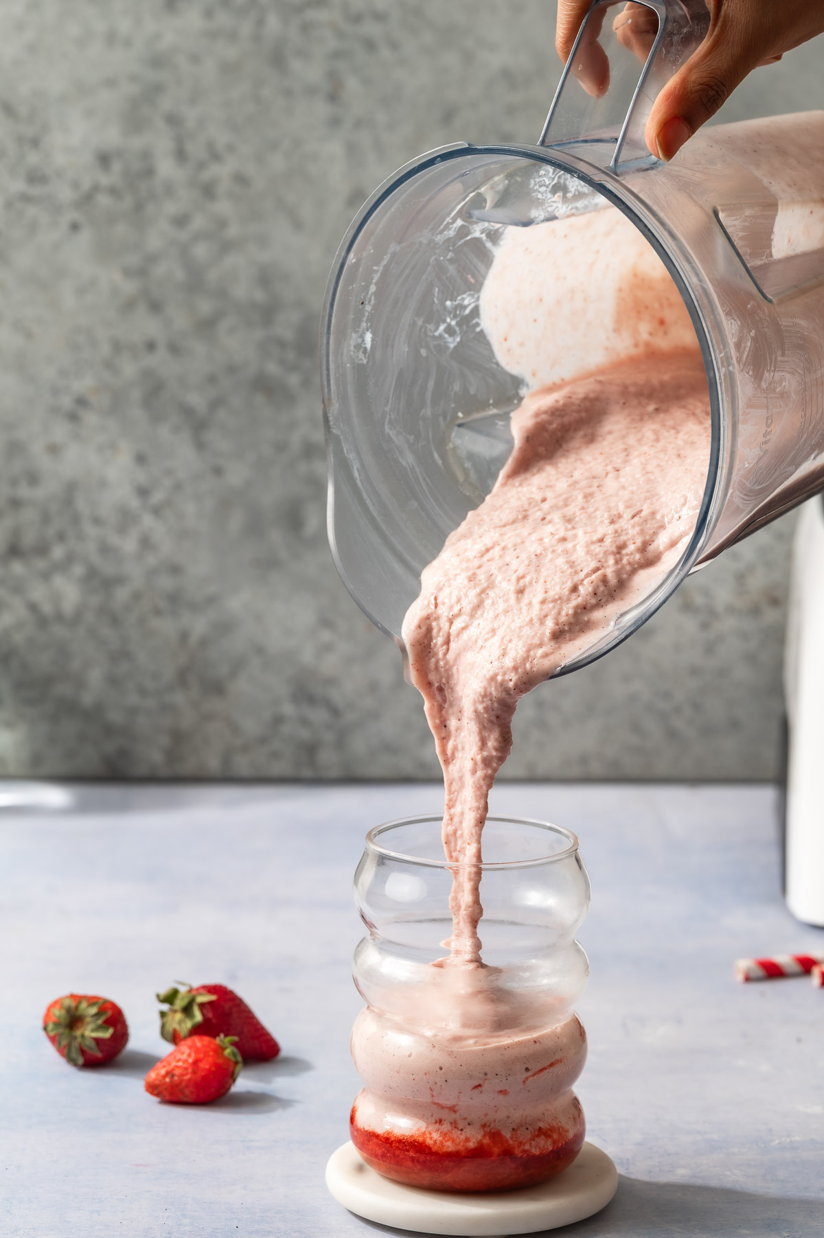 A person pouring strawberry protein shake in a glass