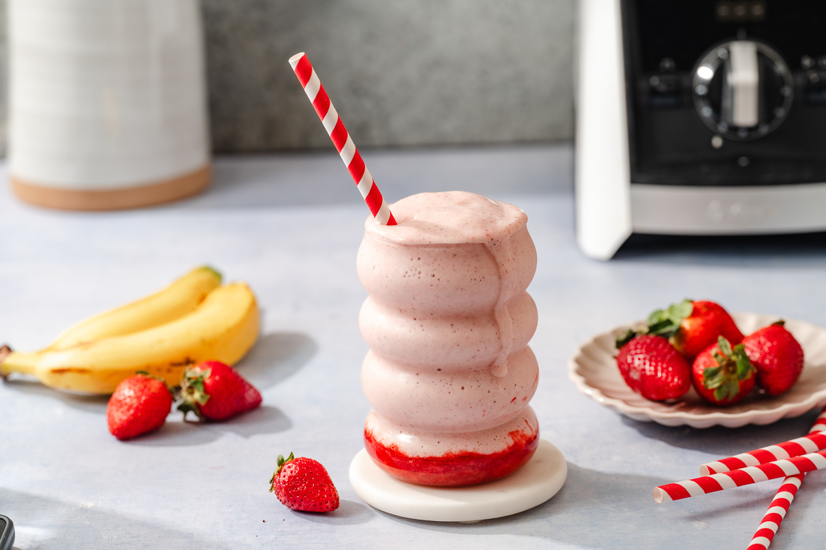 A glass of strawberry protein shake surrounded by strawberries and bananas