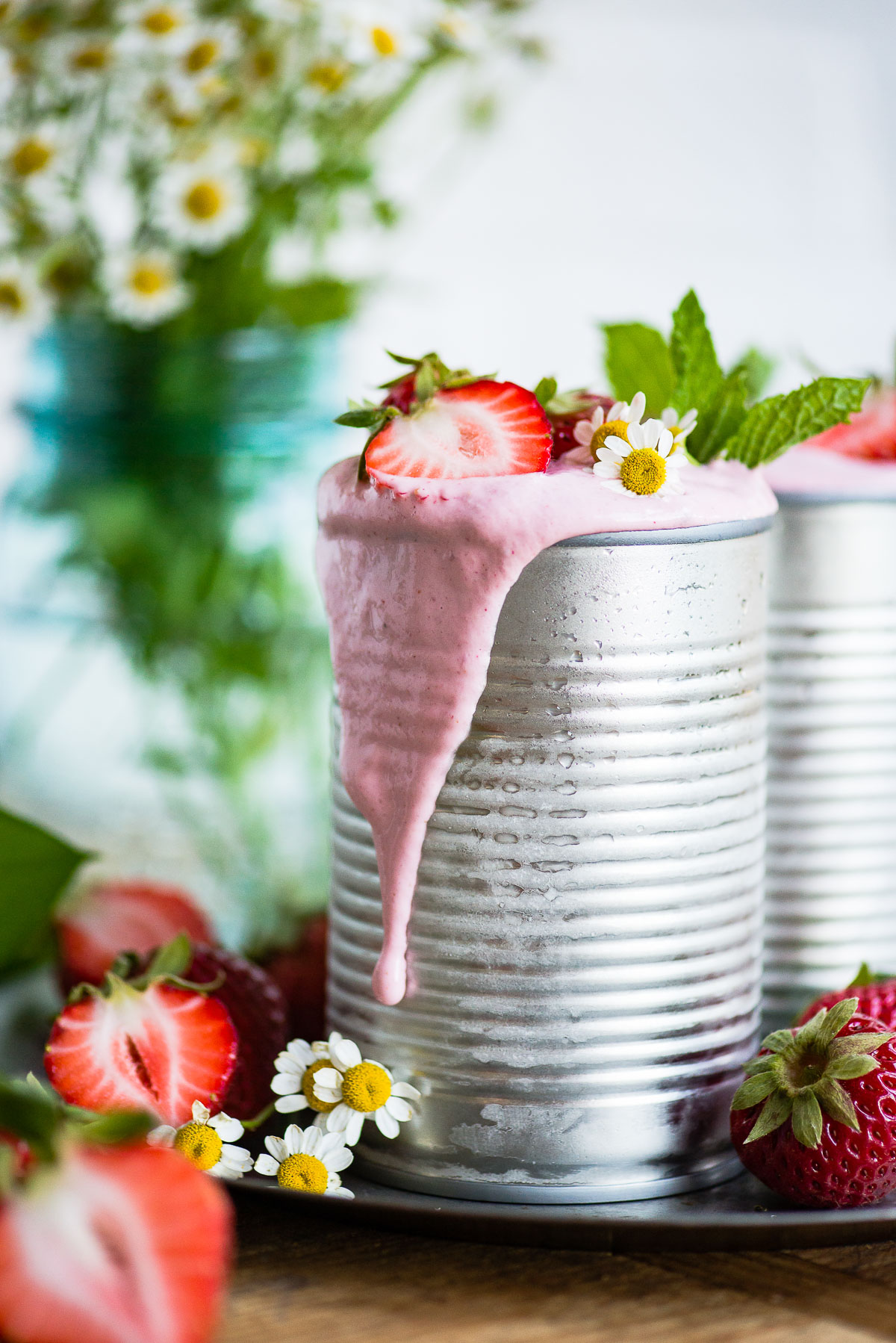Aluminum can overflowing with a delicious, pink vegan strawberry milkshake, topped with fresh strawberries.