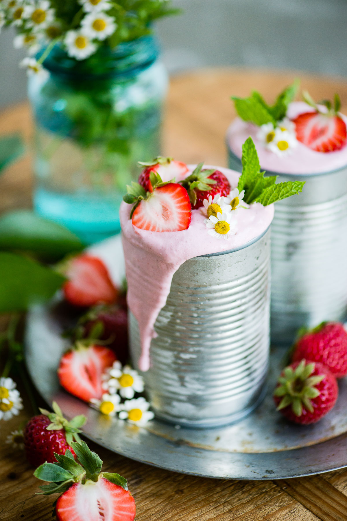 Aluminum can overflowing with a vibrant, pink vegan strawberry milkshake, garnished with fresh strawberries.