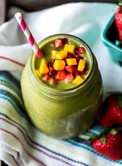 strawberry mango smoothie in glass jar with paper straw and topped with fresh fruit.