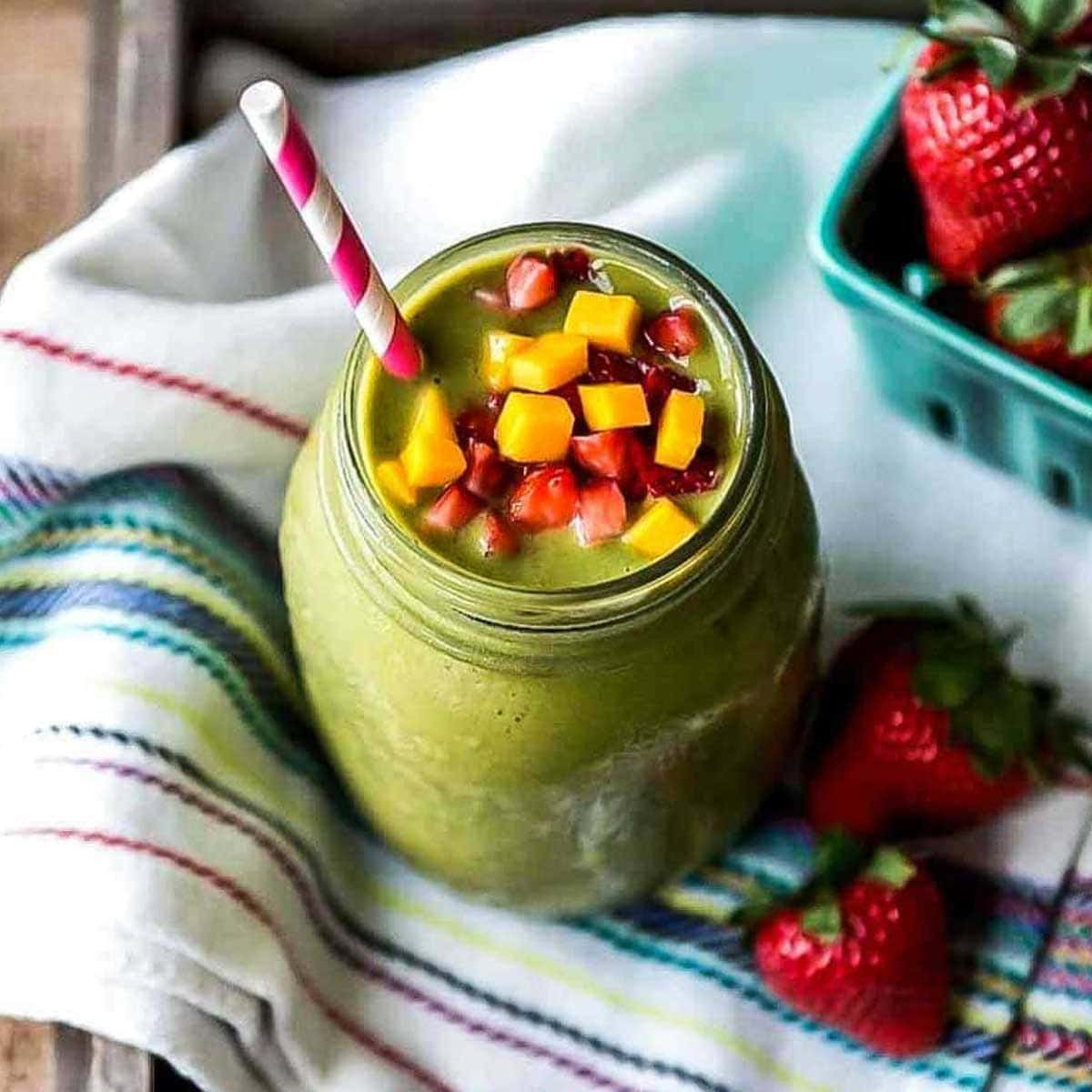 Strawberry mango smoothie in glass jar with paper straw and topped with fresh fruit.