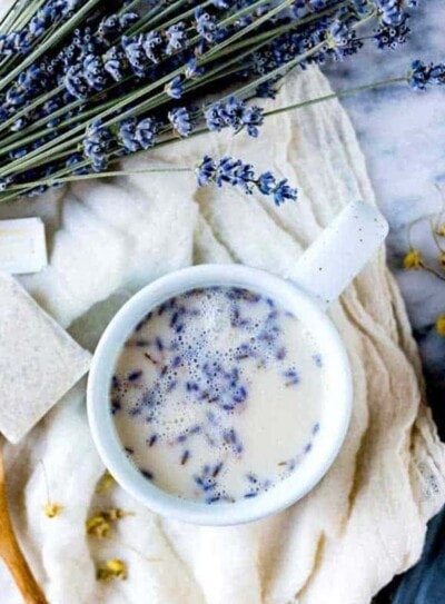 lavender sleep tea buds in a mug of herbal tea on a cloth with a tea bag and fresh lavender.