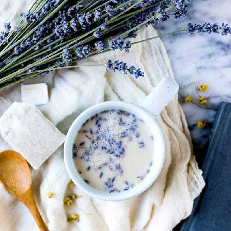 lavender sleep tea buds in a mug of herbal tea on a cloth with a tea bag and fresh lavender.