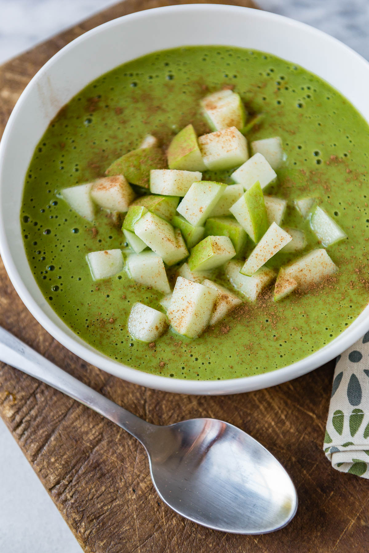 Healthy green smoothie bowl topped with sliced apples and cinnamon.