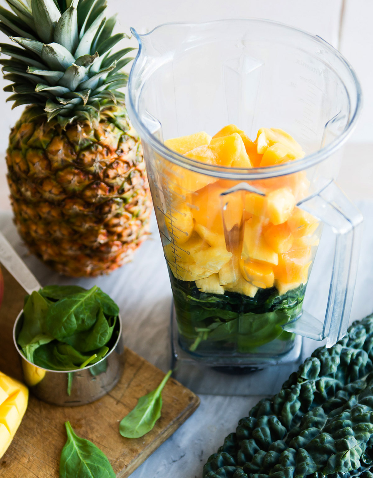 Blender container filled with spinach, kale, mango and pineapple. 
