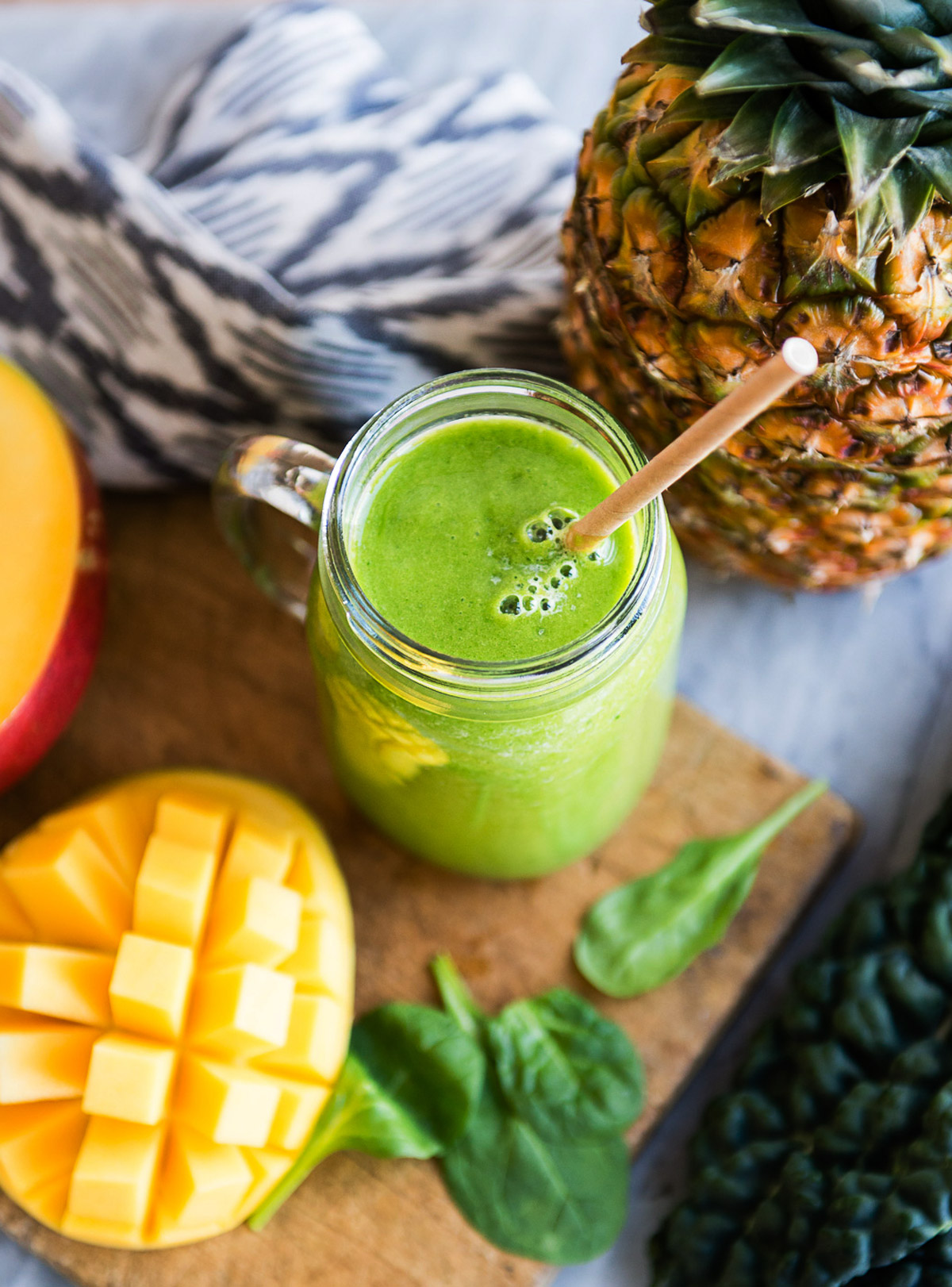 Detox smoothie in a mason jar with a paper straw surrounded by fresh ingredients.