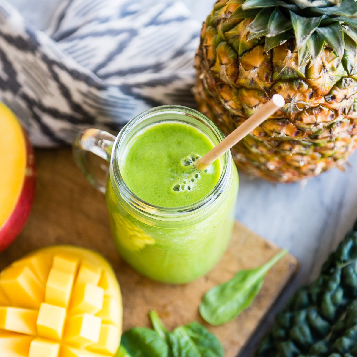 Tropical detox smoothie in a Mason jar surrounded by fresh ingredients.
