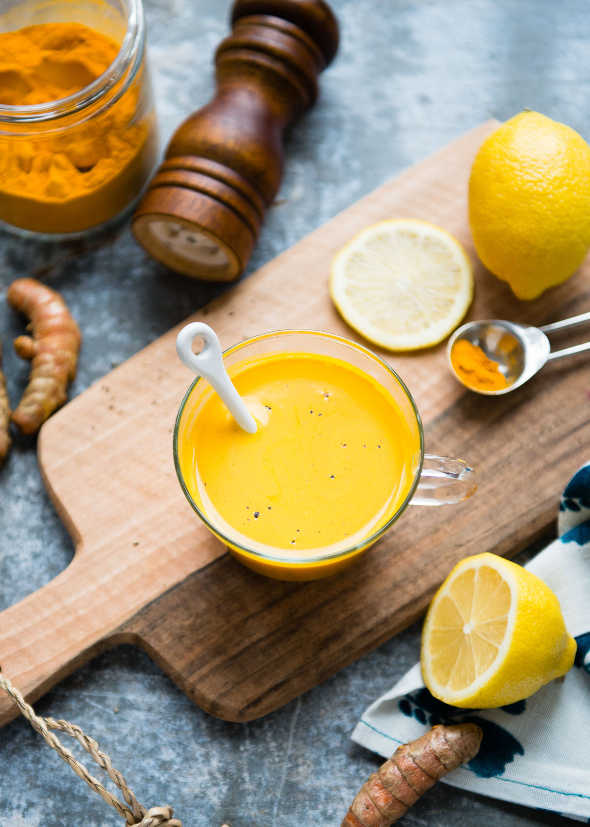 A glass mug of turmeric tea with surrounding fresh ingredients.