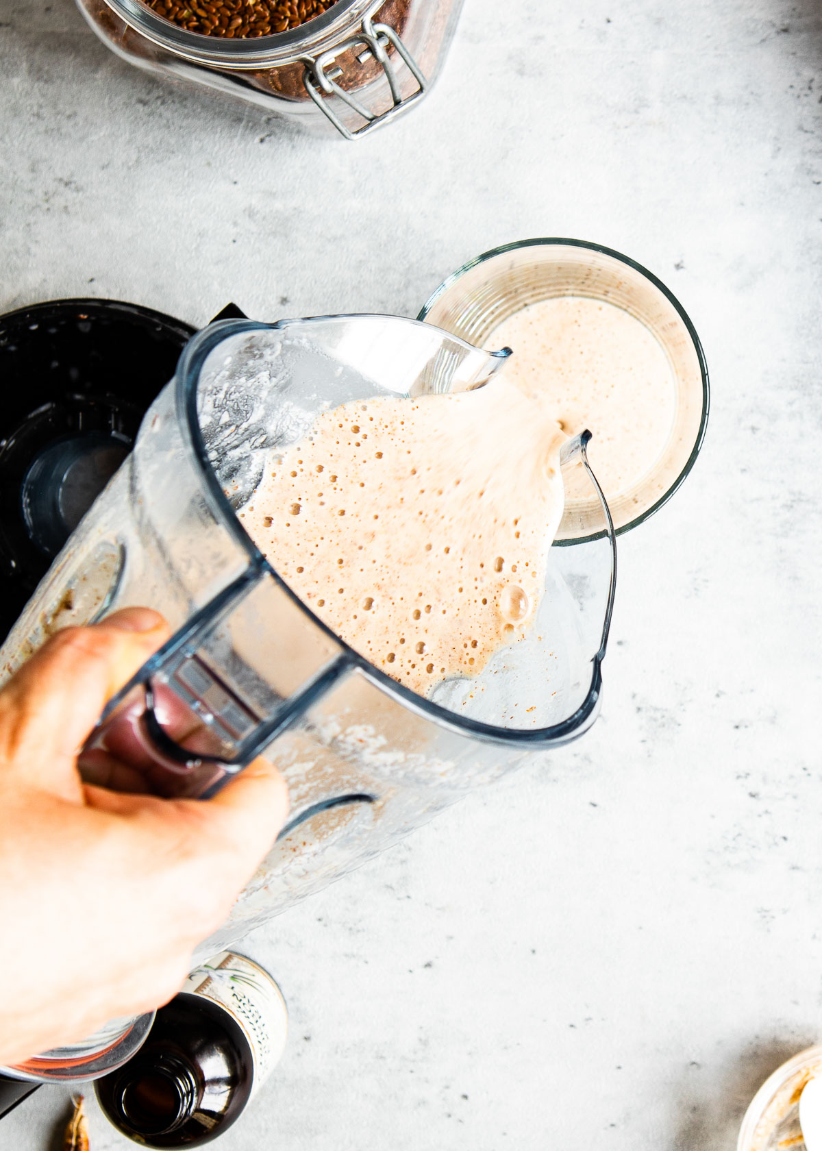 A blender container filled with vanilla flaxseed smoothie being poured into a glass
