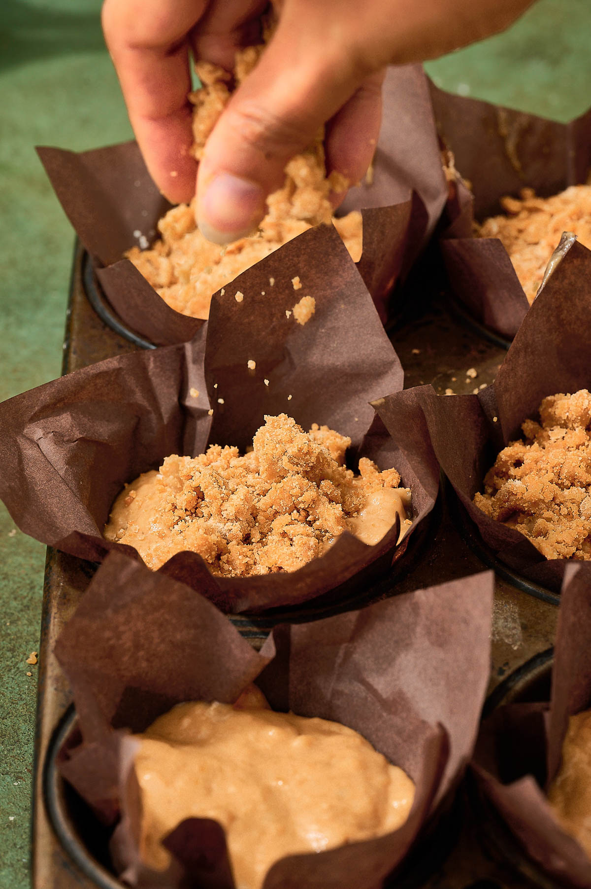 A person filling unbaked muffin batter in parchment-lined muffin cups