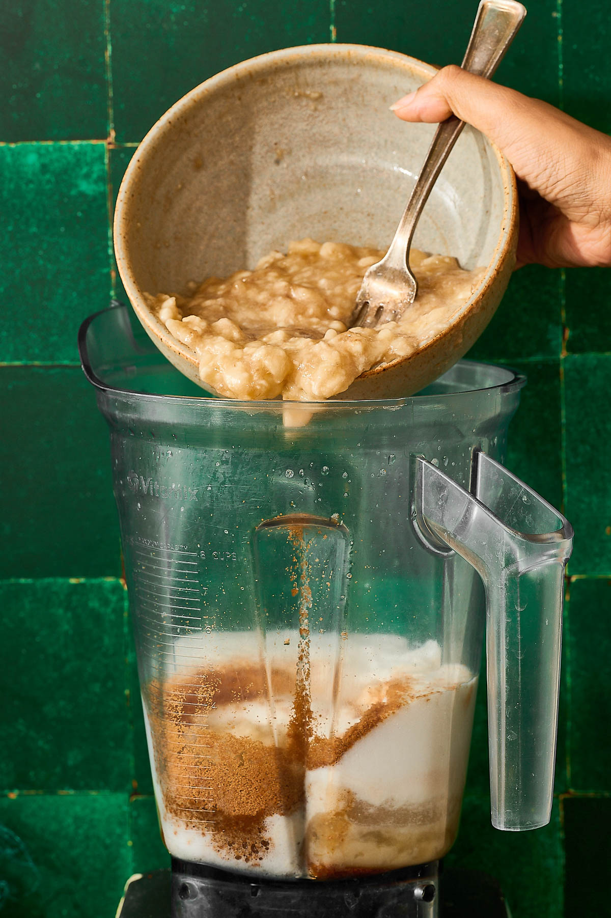 Mashed banana being poured into a blender with other mixed ingredients