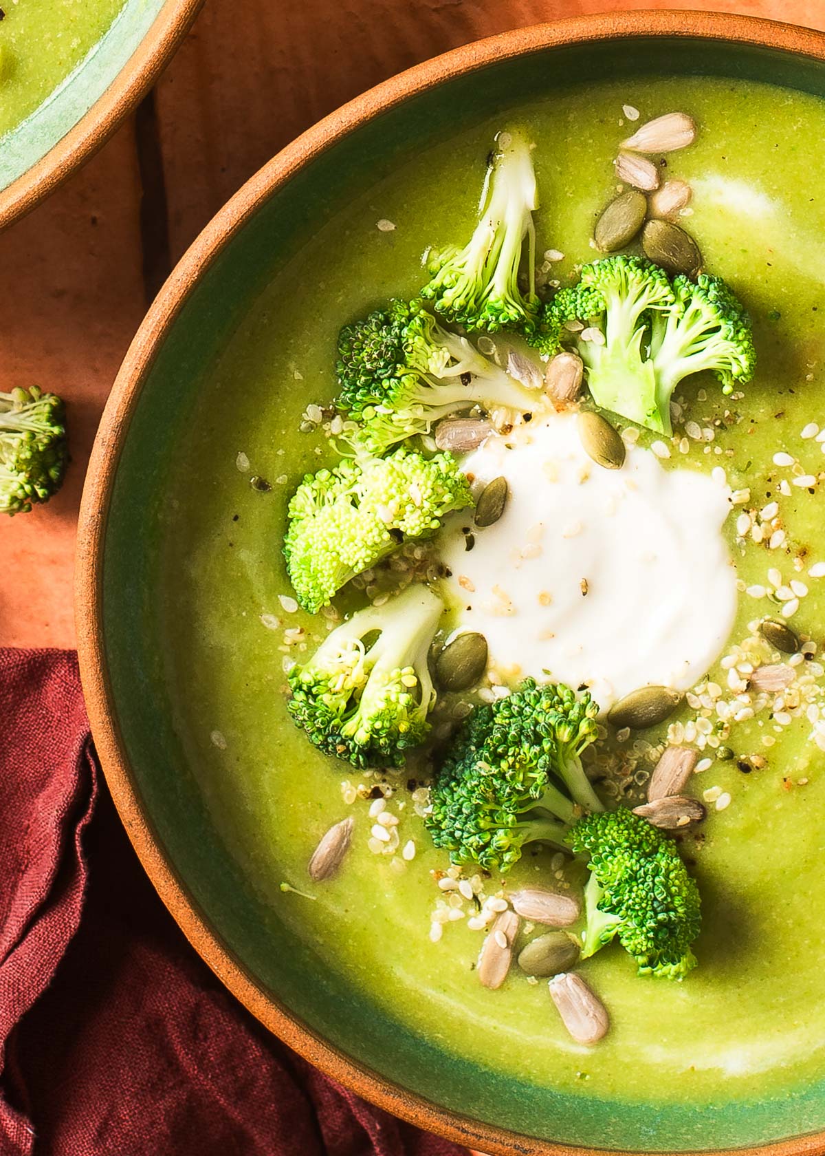 A detailed shot of creamy vegan broccoli soup topped with dairy-free sour cream, fresh broccoli, and sesame seeds.