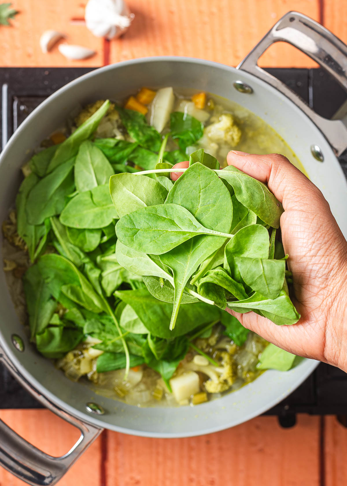 A hand adding fresh spinach to a pot of simmering vegetables.